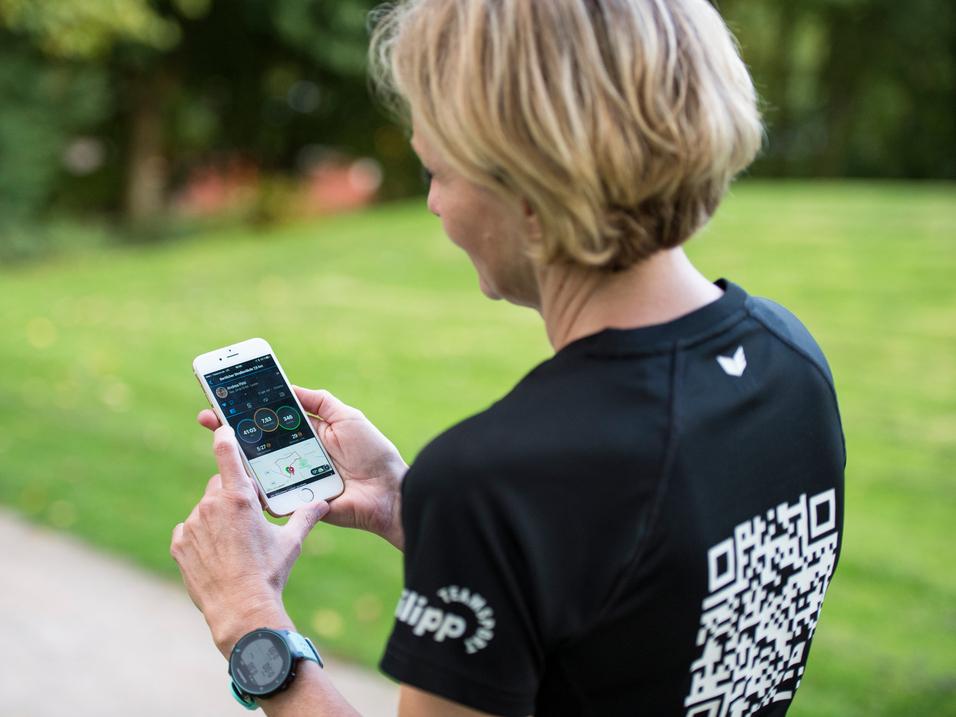 Frau mit kurzen Haaren schaut auf ein Smartphone, während sie auf einem Weg in einem Park steht.