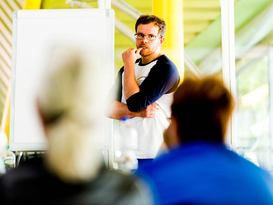 Mann mit Brille spricht vor einer Gruppe, ein Flipchart ist im Hintergrund sichtbar.